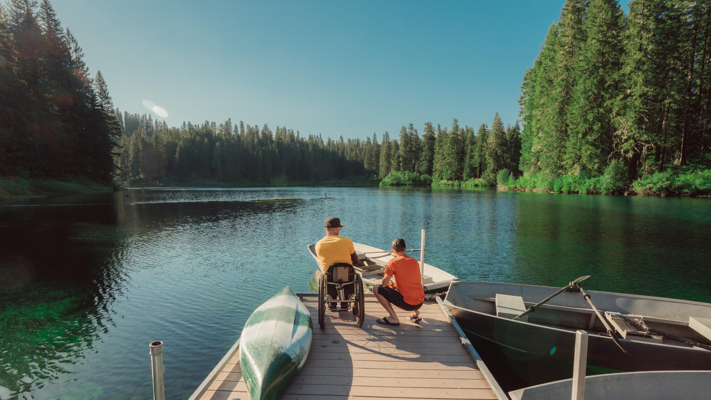 Two people at the end of a dock overlook a large lake.