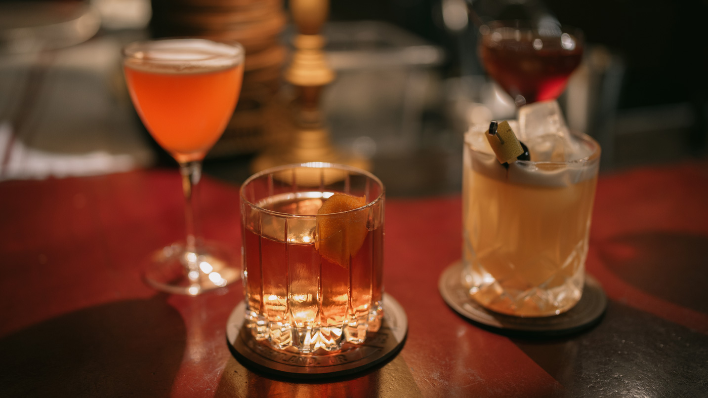 Three cocktail drinks on a bar.