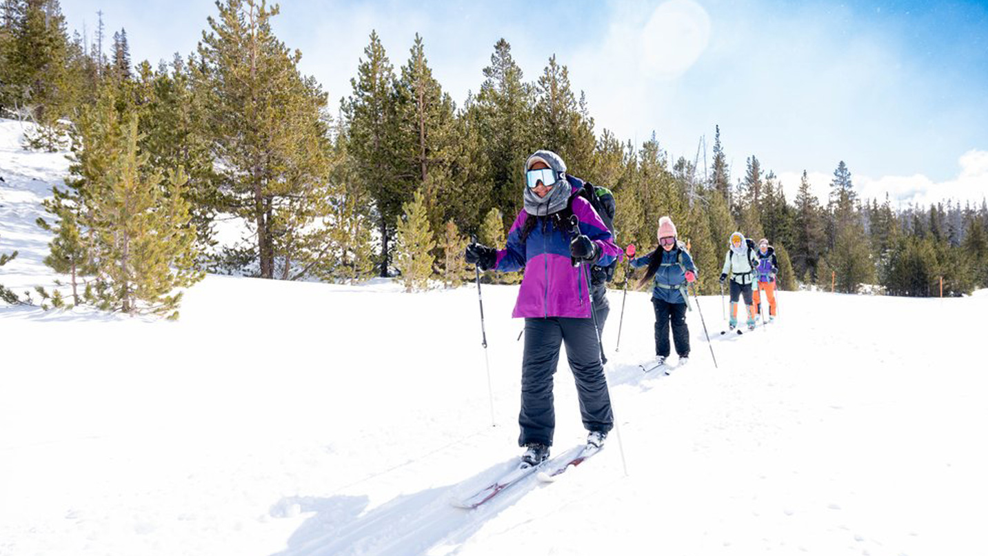 A group of skier single file on a sunny day.