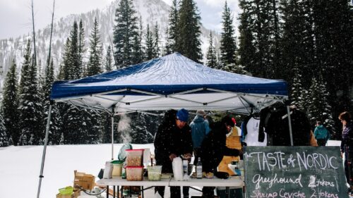 An outdoor tent is set up serving food in front of a scenic snowy mountain backdrop.
