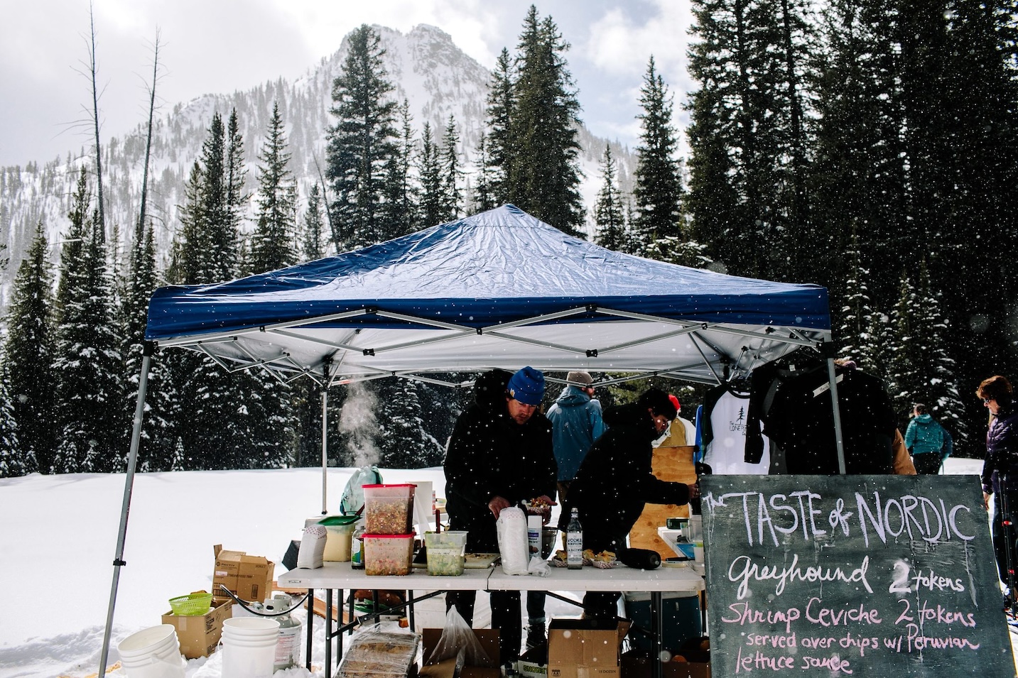 An outdoor tent is set up serving food in front of a scenic snowy mountain backdrop.