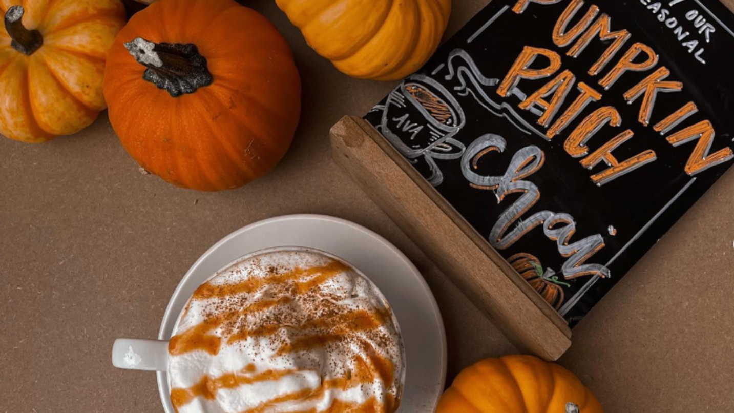 A coffee drink topped with whip cream and pumpkin syrup, surrounded by pumpkins.