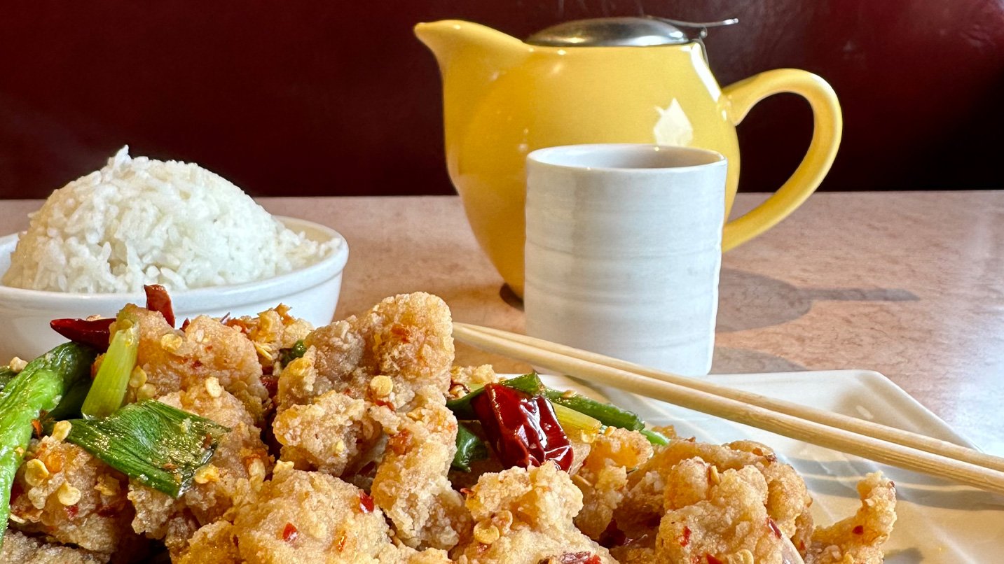 Close-up plate of fried food with bowl of rice, tea pot and tea cup