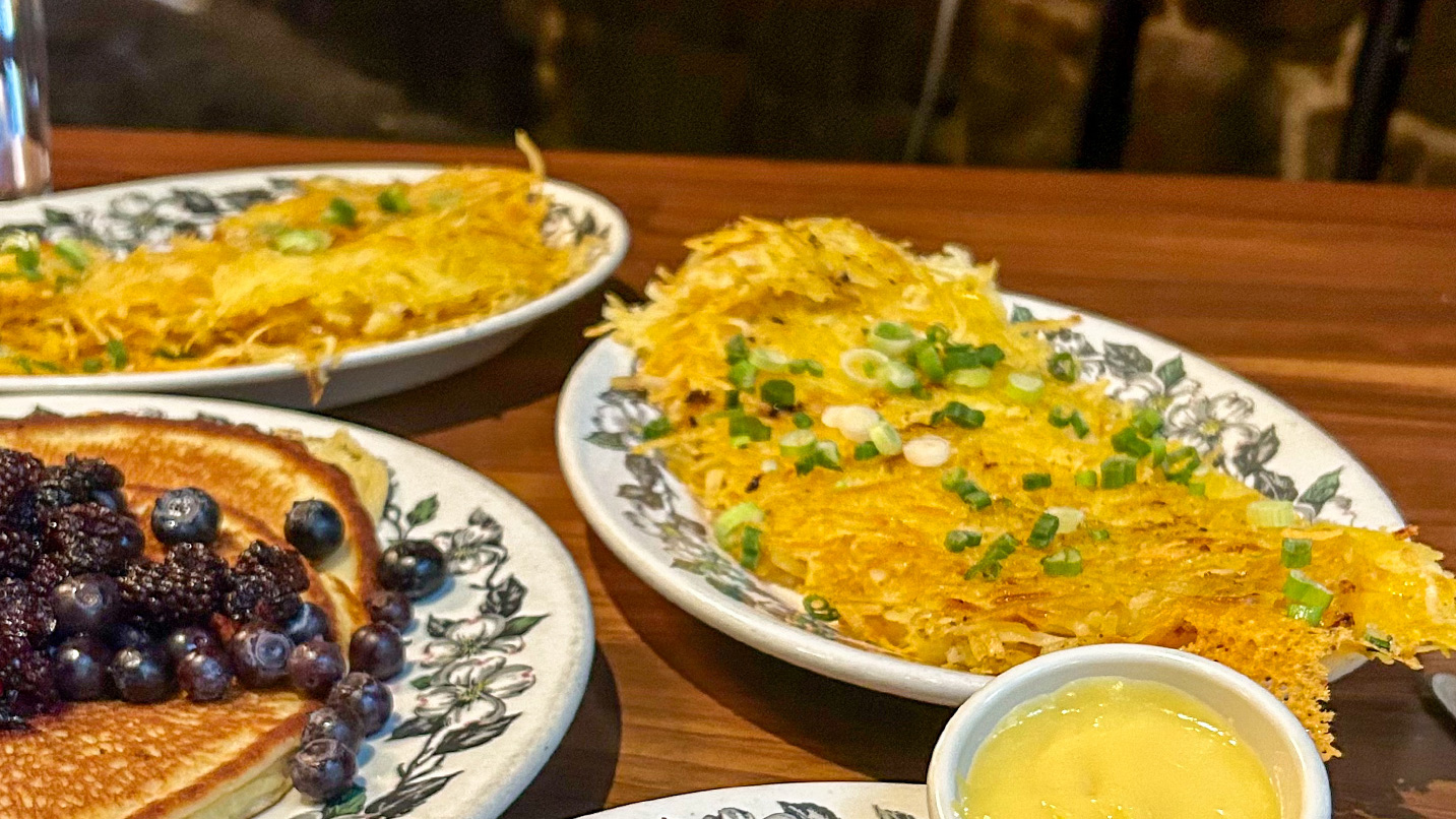 Plates of hashbrowns and blueberry pancakes.