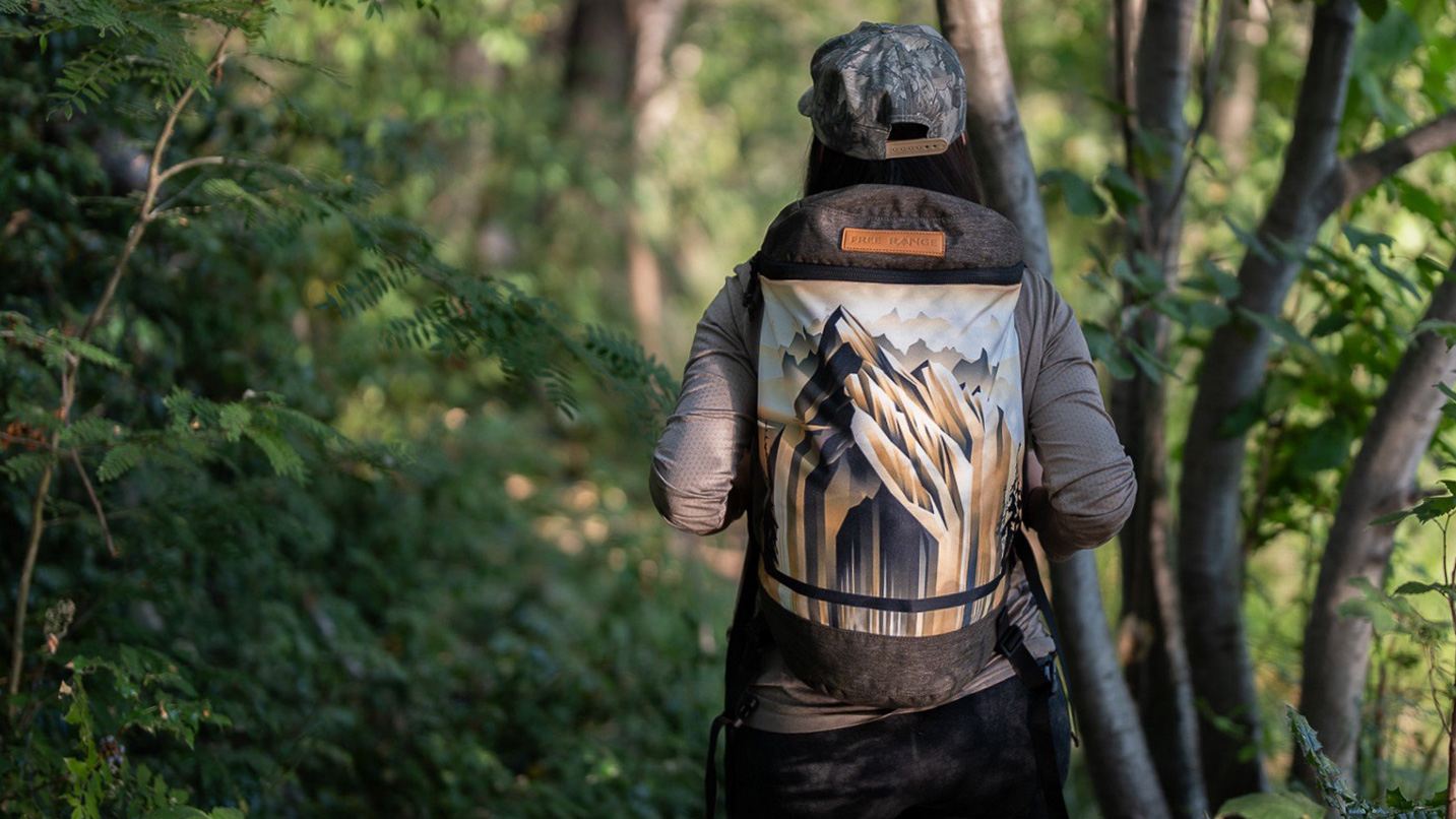 A canvas outdoor backpack with artwork of a mountain being worn by a person.