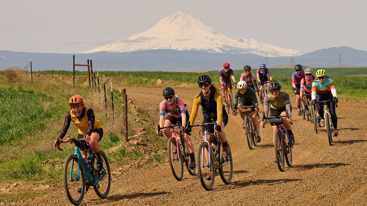 Bicyclists on a gravel road against a mountain backdrop.