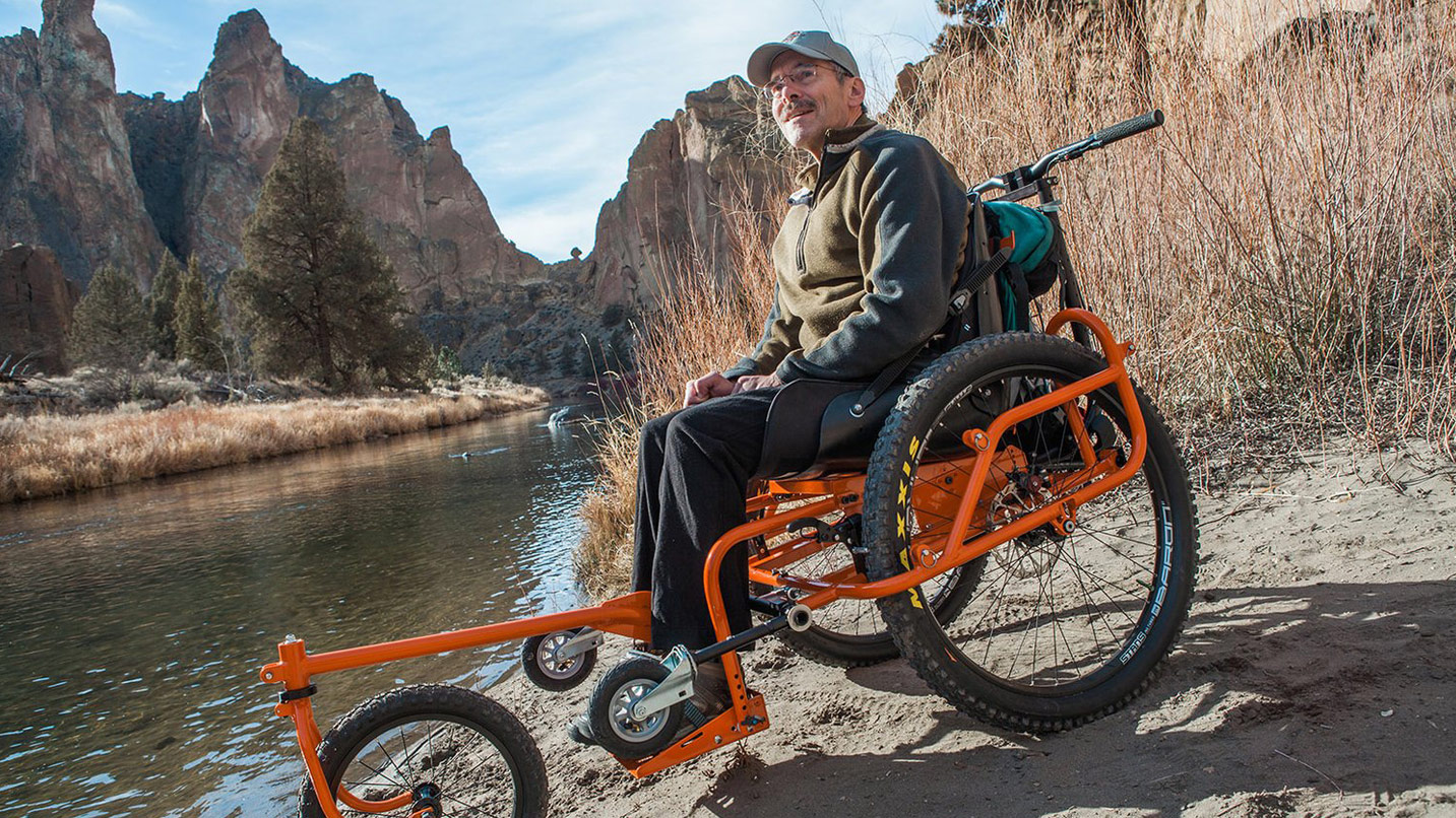A man in a specialized wheelchair with an extra wheel in front for maneuverability.