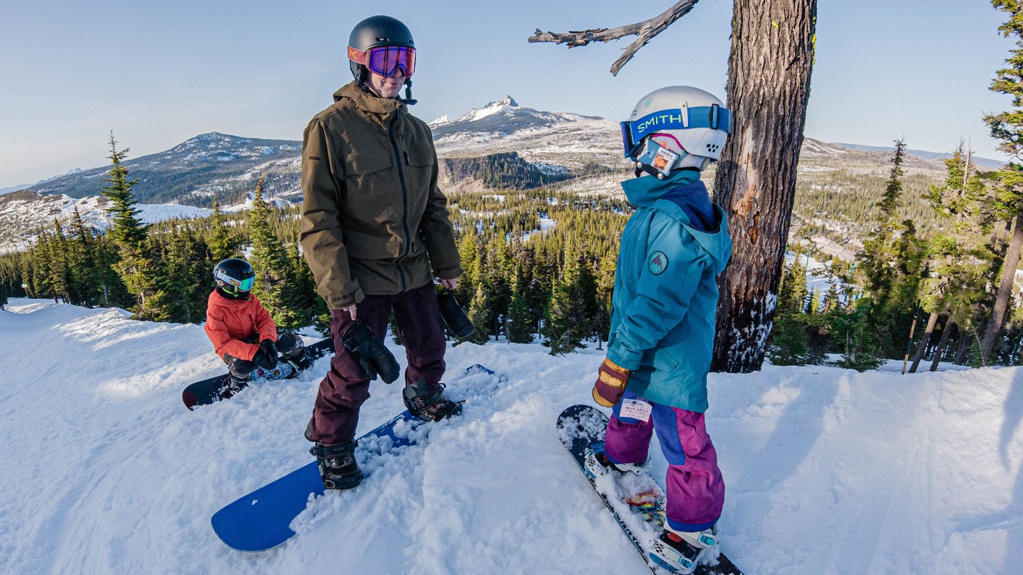 An adult and two kids on snowboards.