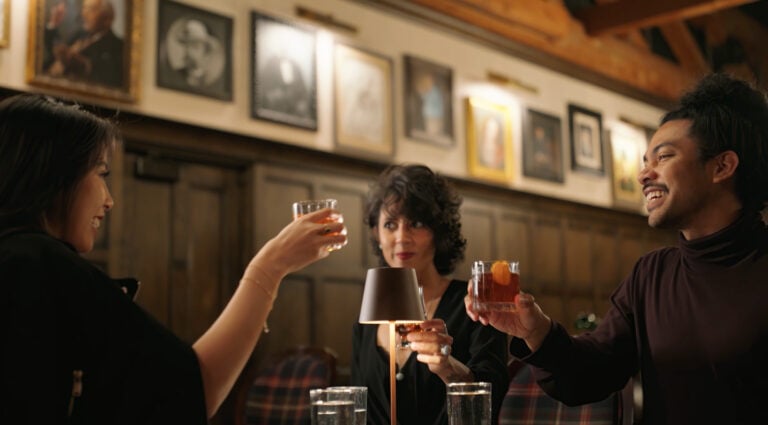 People at a table holding up glasses of whiskey.