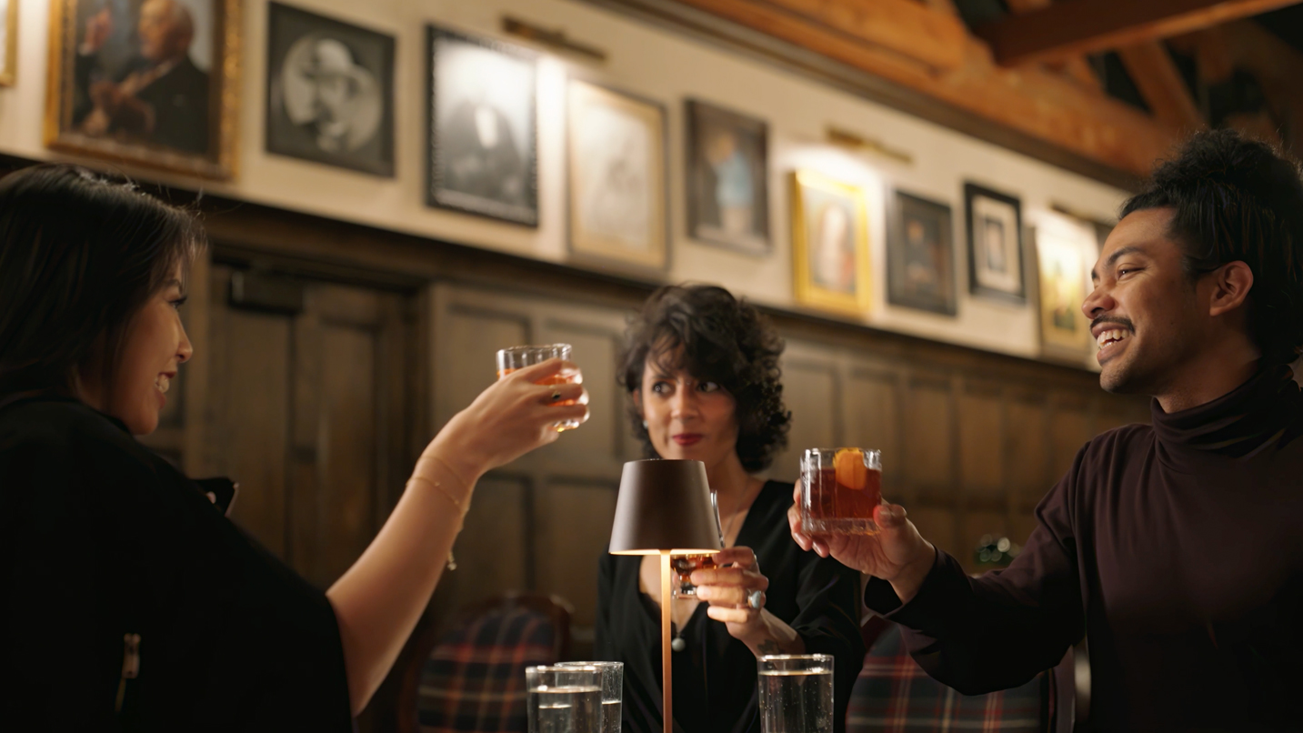 People at a table holding up glasses of whiskey.