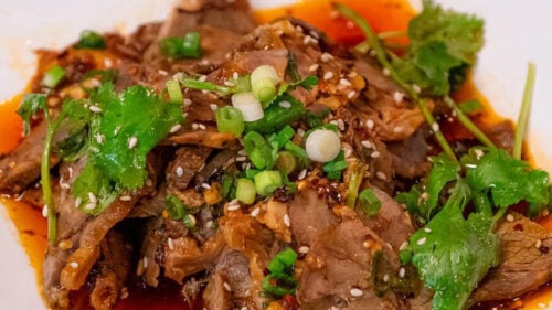 Meat, sauce, green onions and cilantro on white square-shaped plate