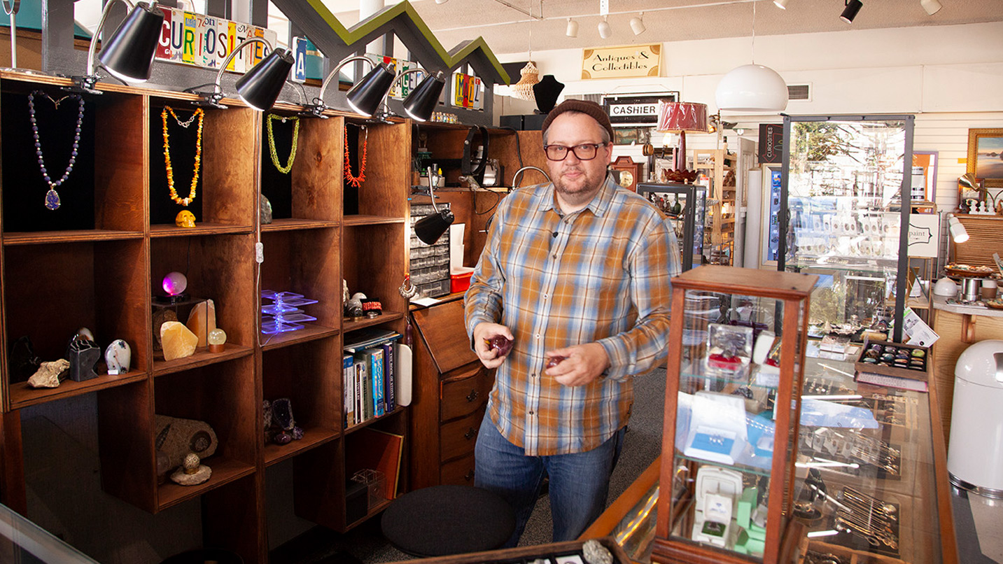 A man stands beside a row of antiques.