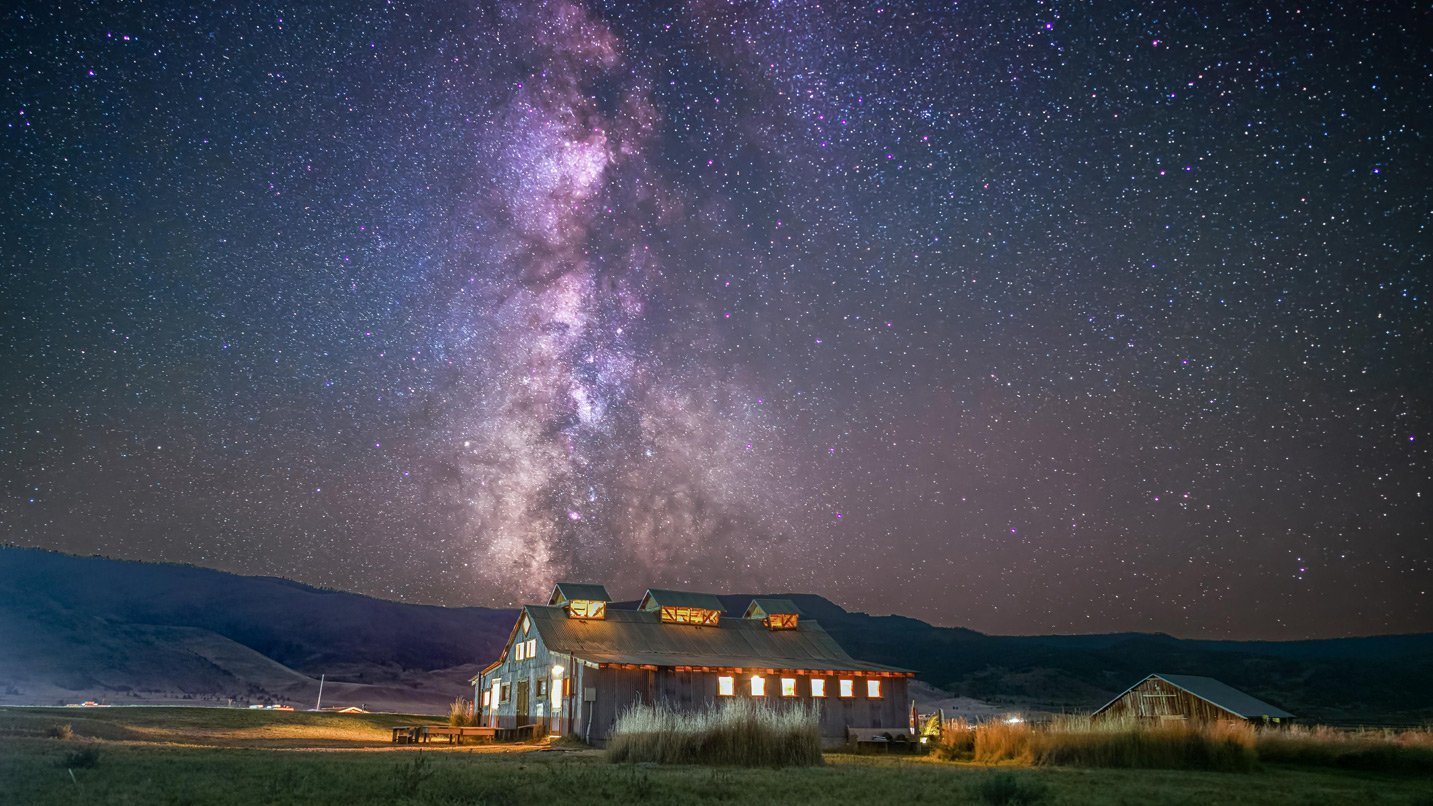 A rustic lodge set against the backdrop of the milky way and thousands of stars.