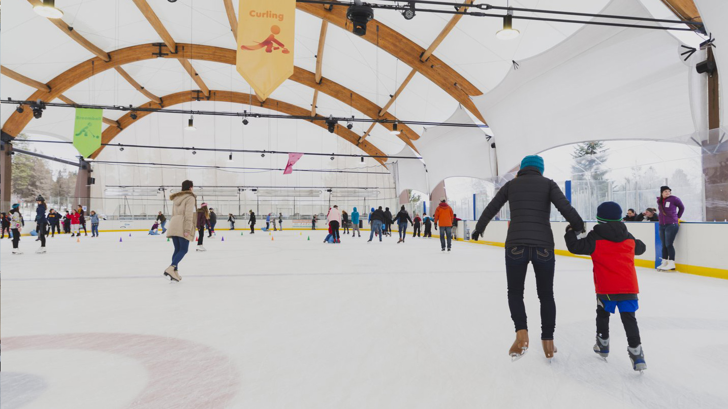 Adults and children ice skating in a covered outdoor rink.