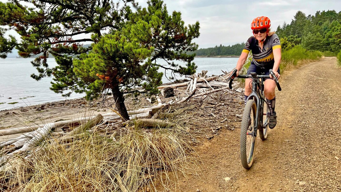 A person bikes on a gravel road next to a body of water.