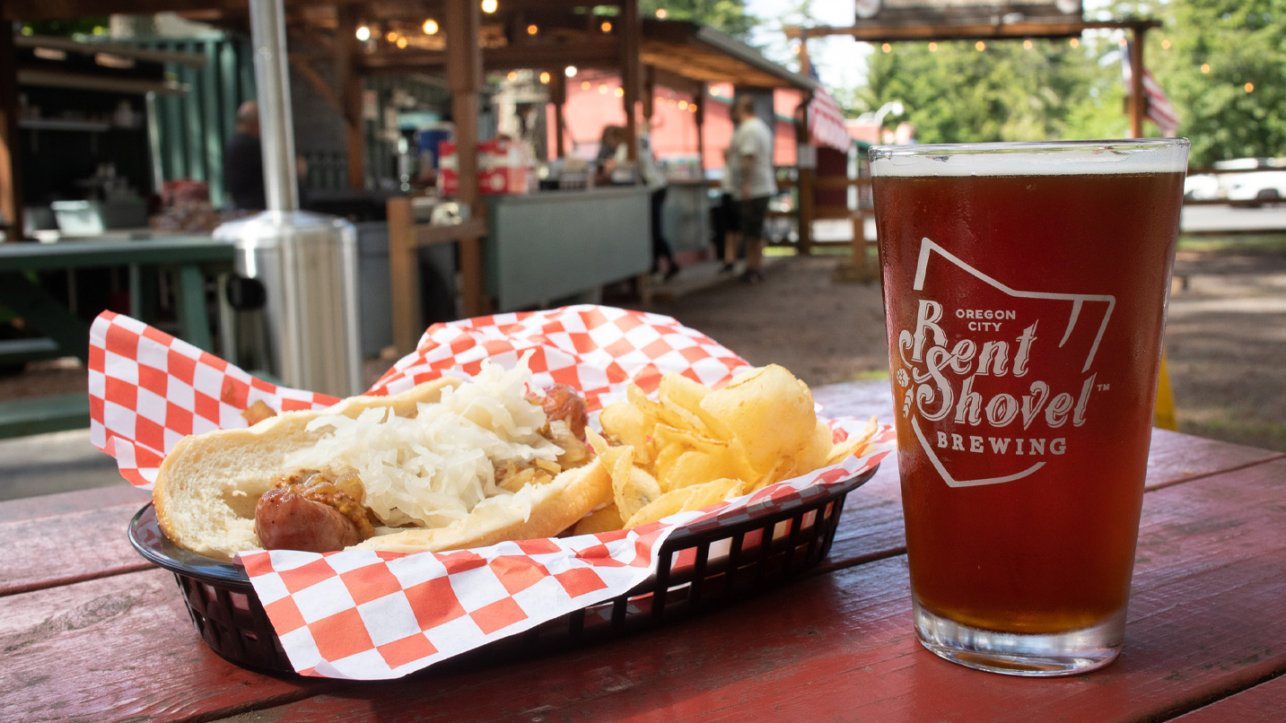 A glass of beer from Bent Shovel Brewing in Oregon City on a table next to a hot dog and chip basket.