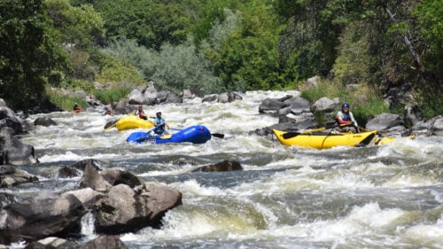 Multiple rafting boats navigate a narrow canyon of rapids.