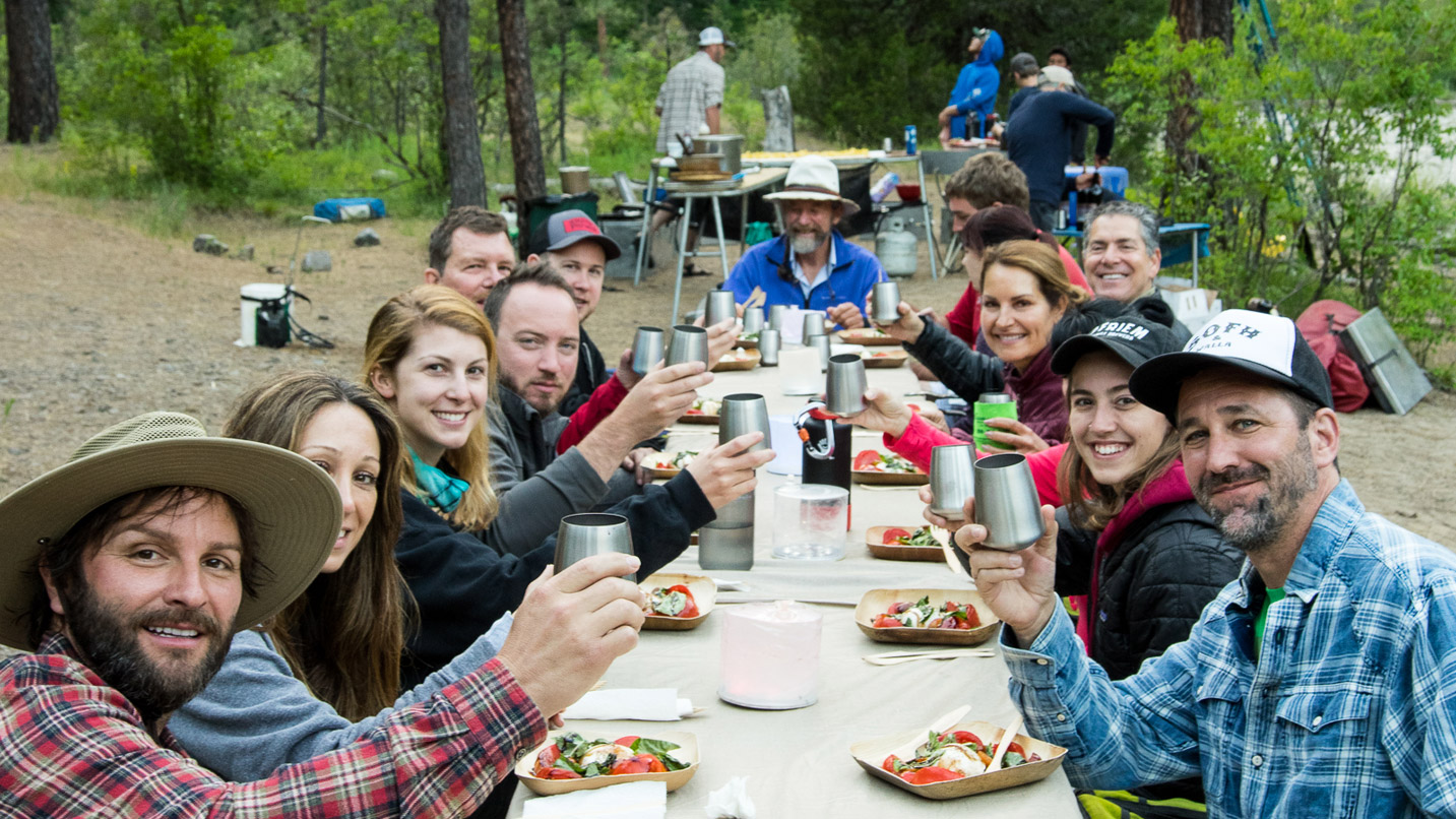 A group of people dine next to a riverbank.