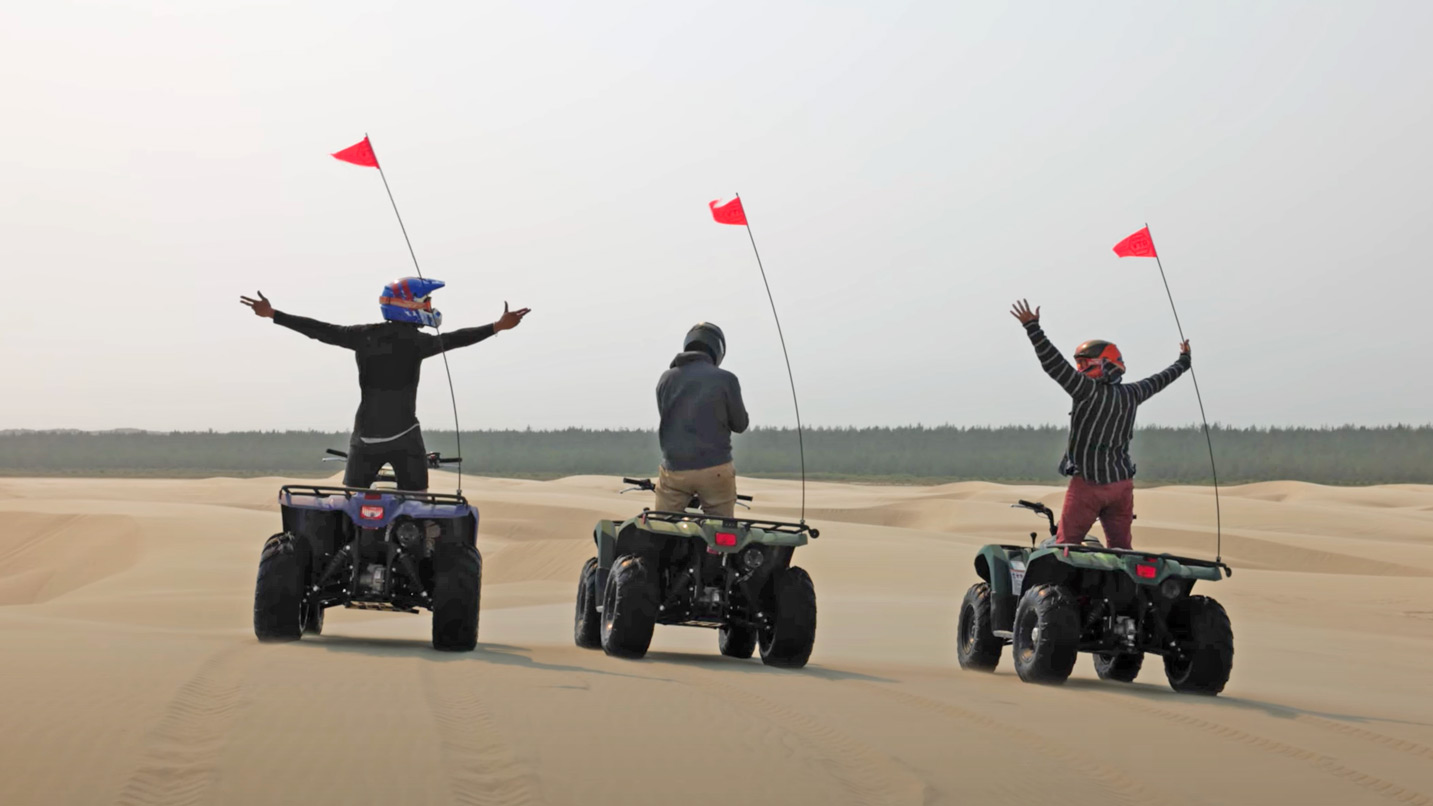 Three men raise arms on ATVs on large expanse of sand