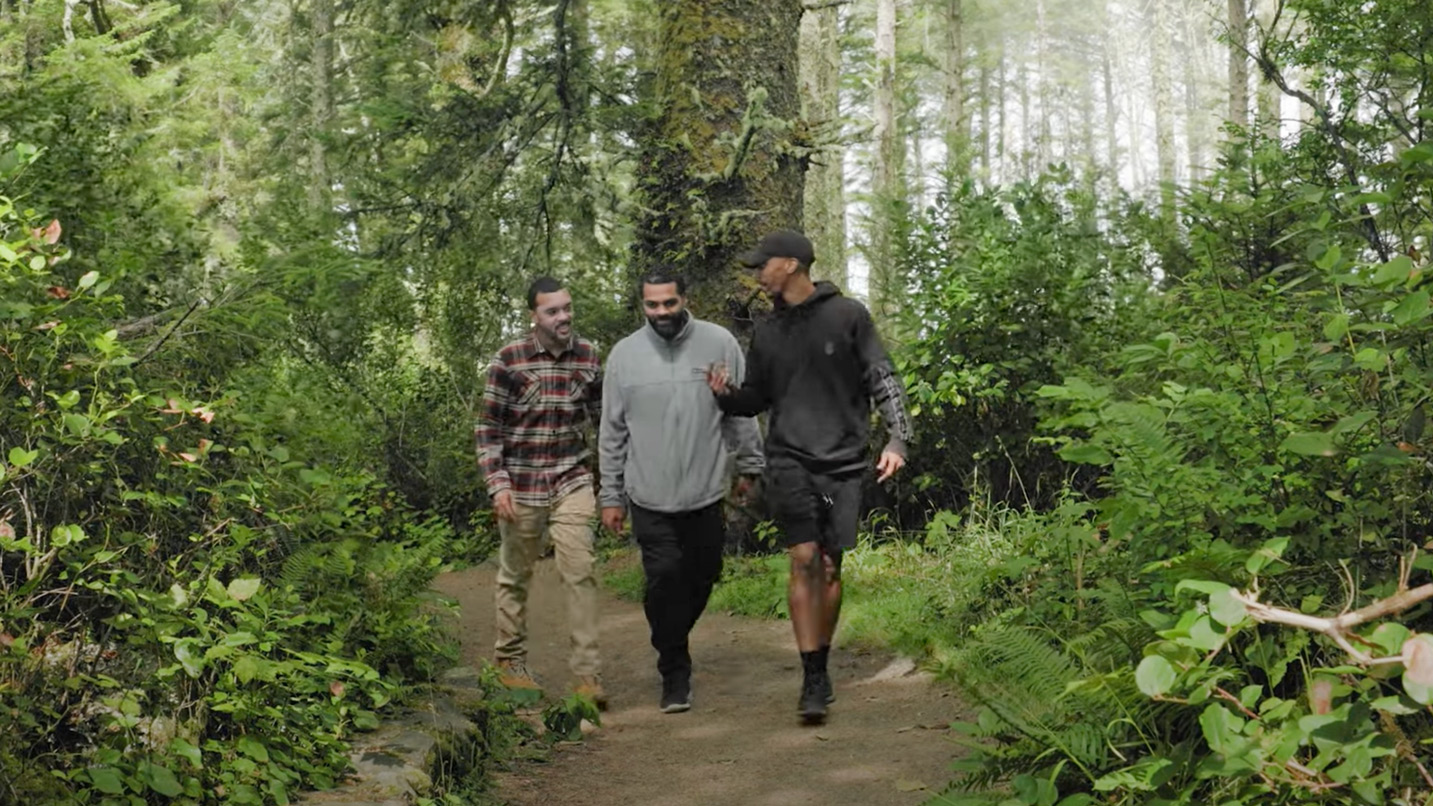 Three men walk on dirt path in forest