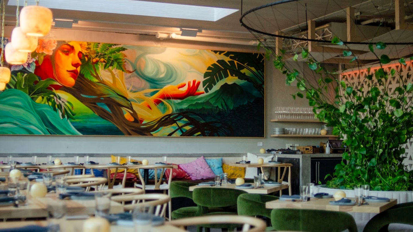 Colorful mural of a woman above soft seating and live plant in a restaurant