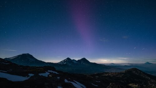 Dark blue night sky with stars over mountain range and a bit of snow