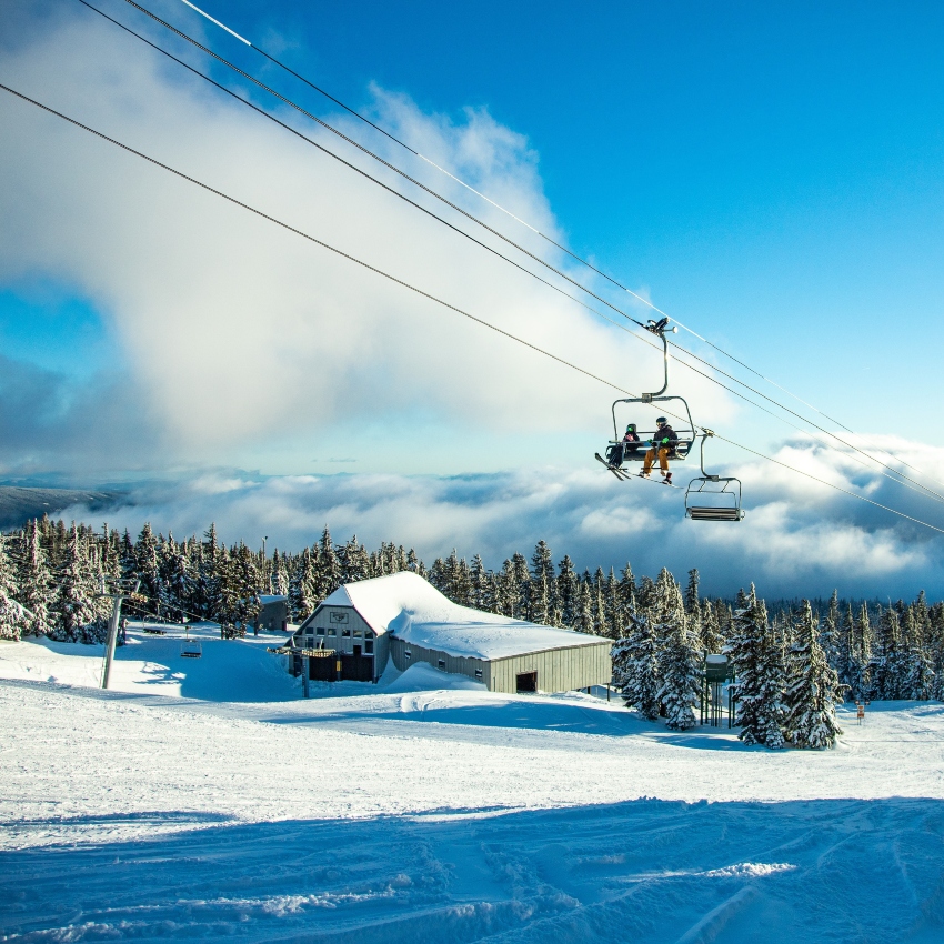 Two people sit on ski lift against field of snow and blue sky