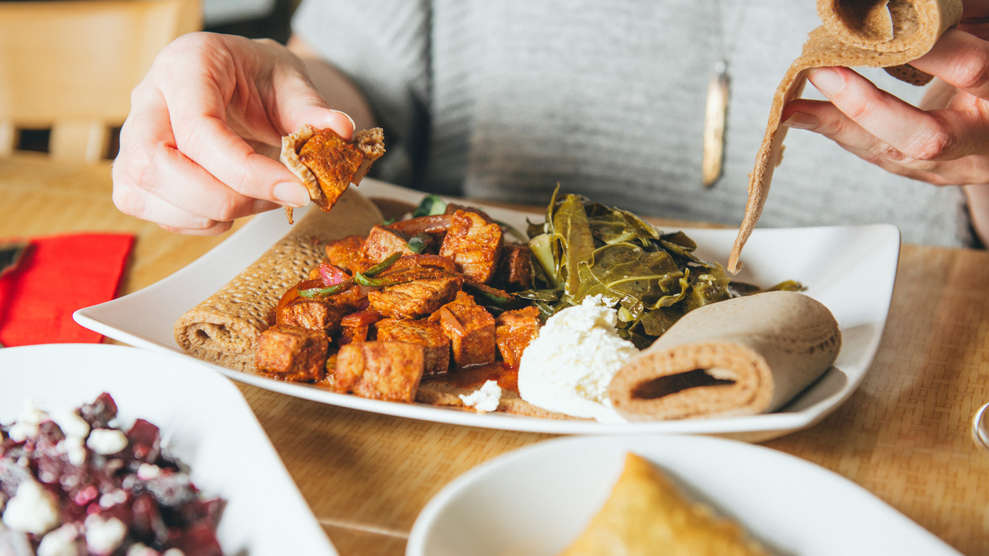 A plate of Ethiopian food, including collard greens, soft cheese, stewed chicken and injera, a type of flatbread.