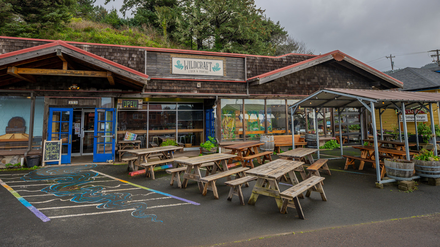 Exterior of a WildCraft's storefront, with colorful murals on the pavement near outdoor picnic seating.
