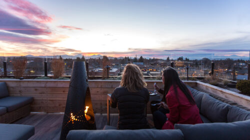 Two people on a rooftop lounge drinking wine and enjoying a sunset.