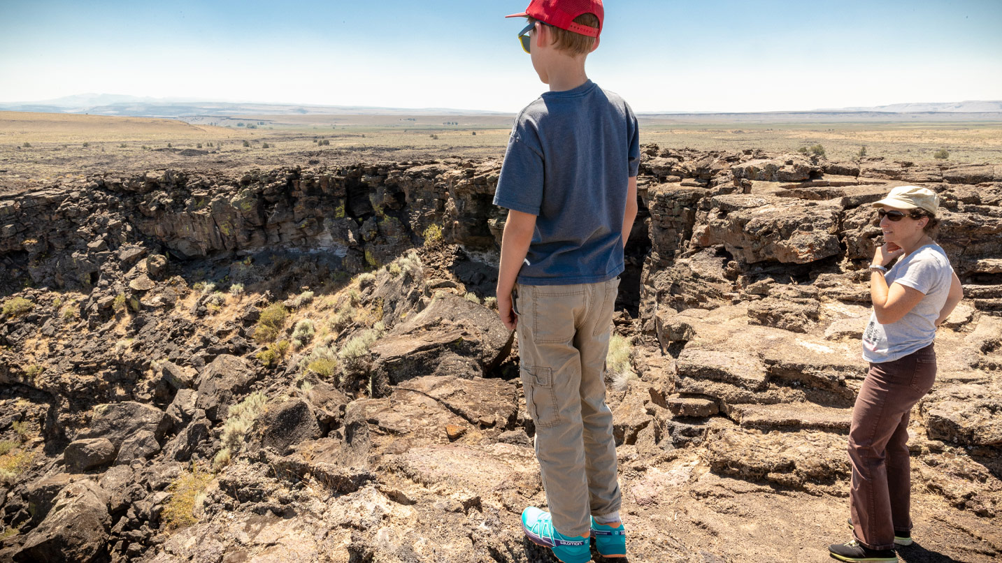 A young boy and woman overlook a crater in the high desert.