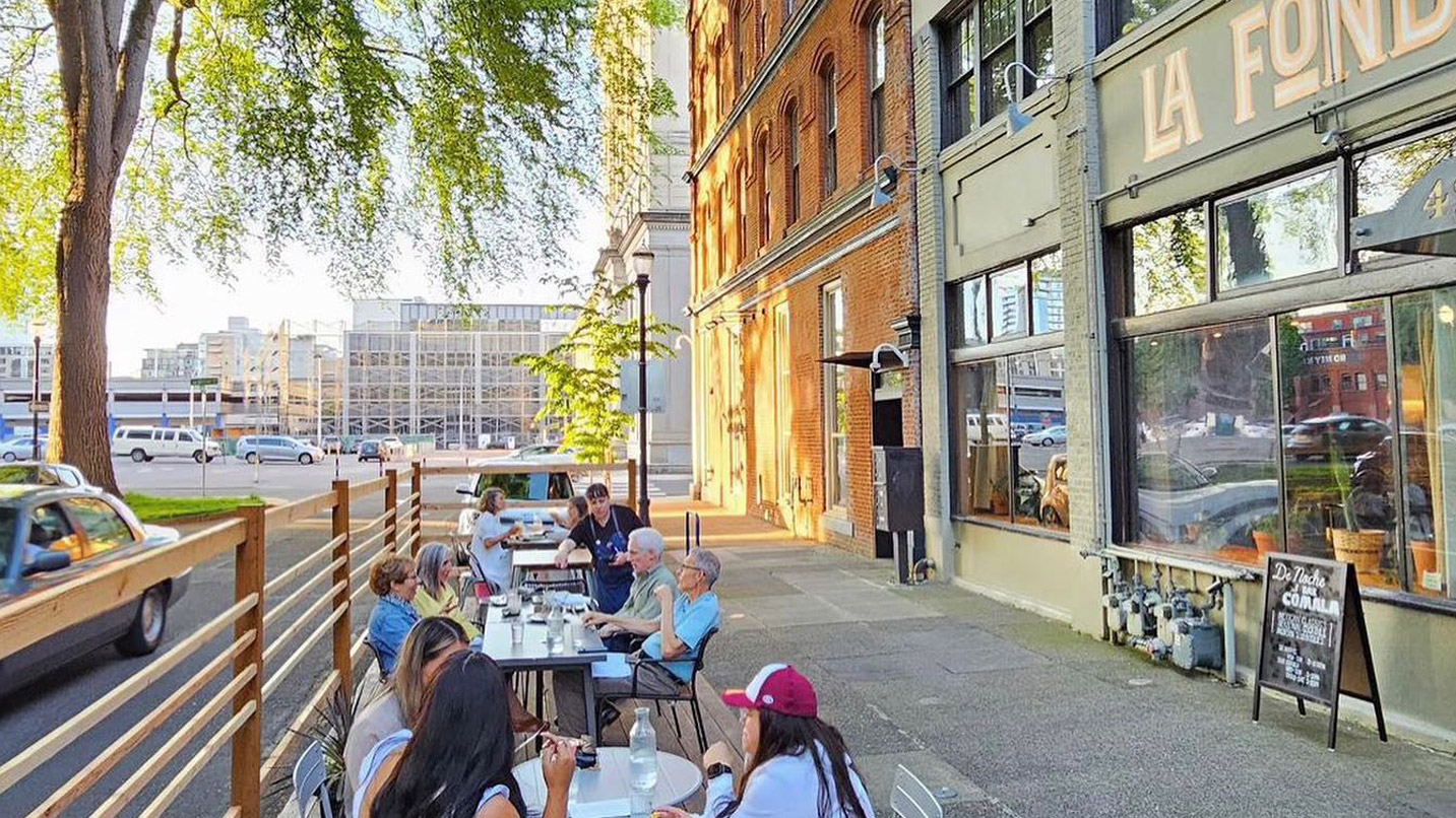 People enjoying a streetside patio on a sunny day.