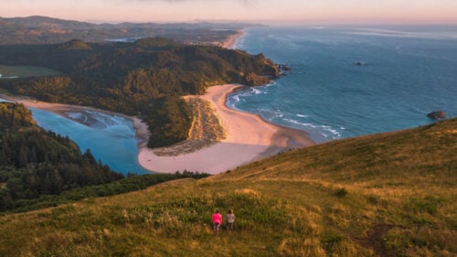 Aerial view of two people on a hill overlooking the ocean.