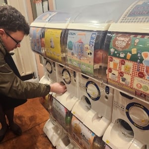 Man kneels down to take something out of a white machine with Japanese words and pictures on it