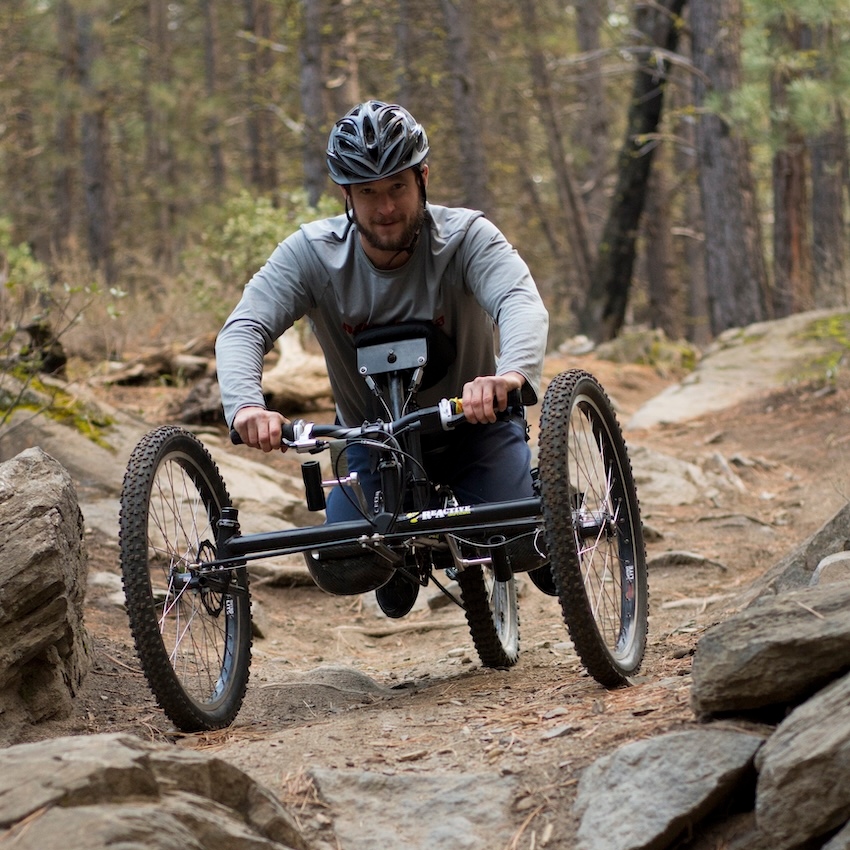 An adaptive mountain biker navigates an expert dirt trail.