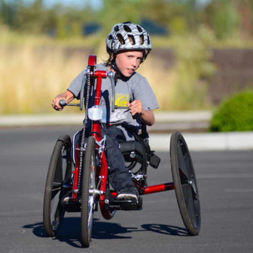 A boy wears a helmet and sits on an adaptive bike with three large wheels.
