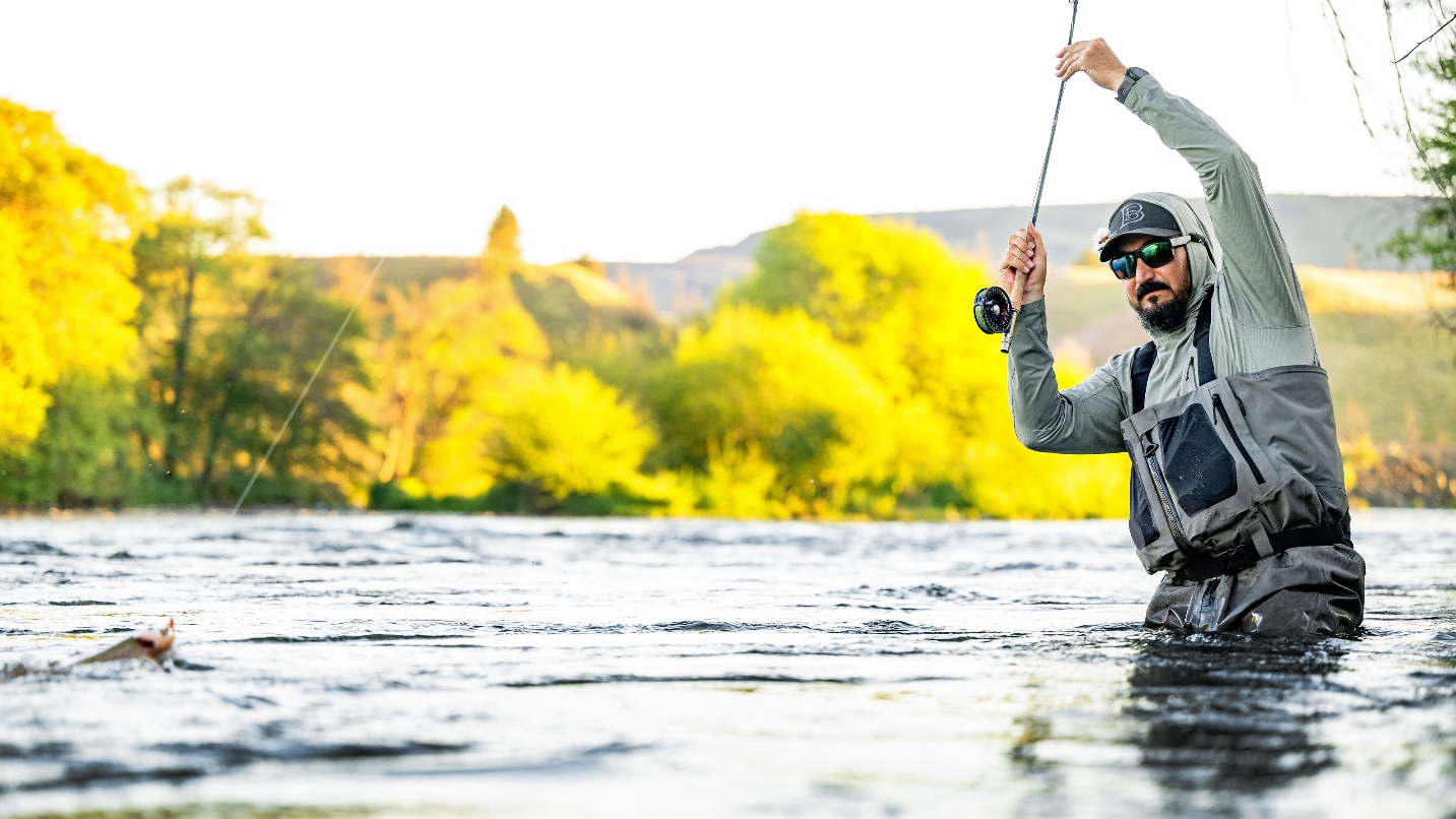 Fisherman stands waist-deep in river holding fishing rod up high