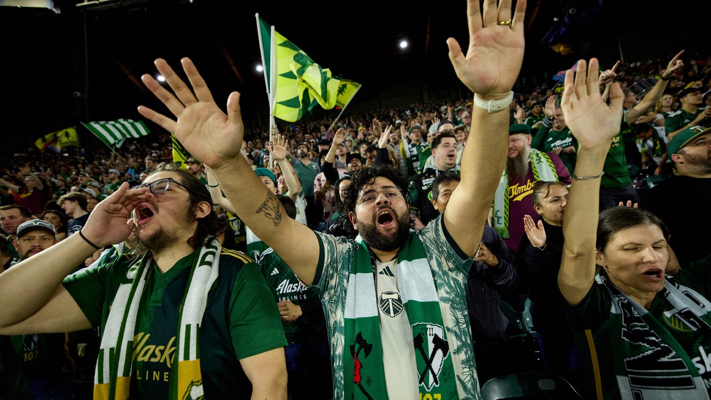 A group of soccer fans in green Timbers gear cheering.