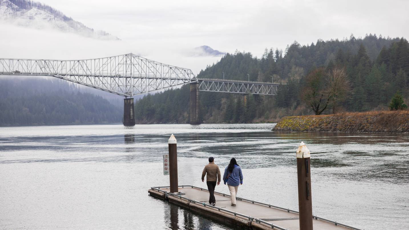 Two people on a dock looking at a view of a bridge.