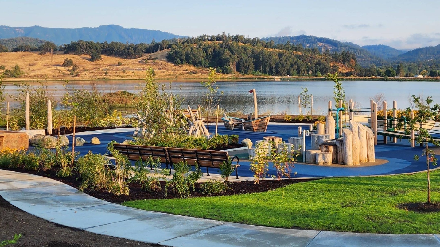 Playground with lake and tree-lined hilltop in background, and flat path in foreground