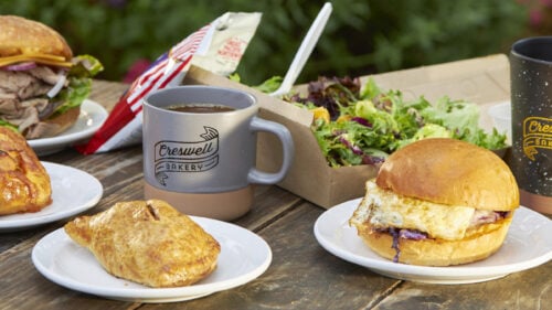Several pastries, sandwiches and mugs emblazoned with Creswell Bakery on a table.