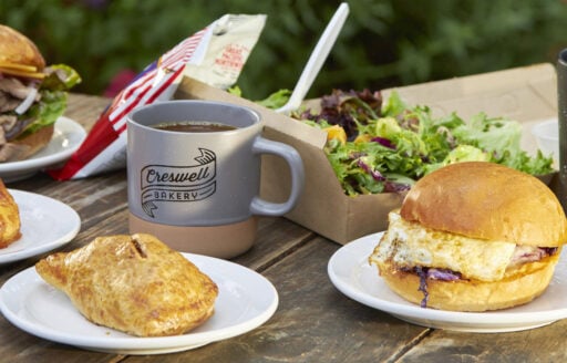 Several pastries, sandwiches and mugs emblazoned with Creswell Bakery on a table.