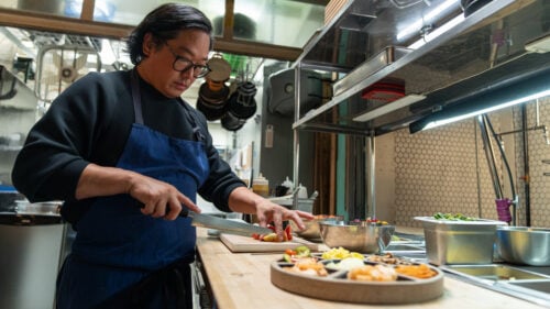 A chef slices vegetables to plate on a dish in his kitchen workstation.