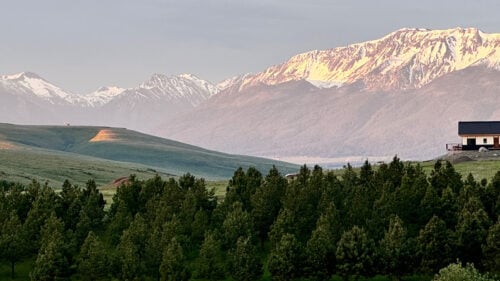 Landscape of hills, firs, mountains and a lone Japanese-style home in the distance.