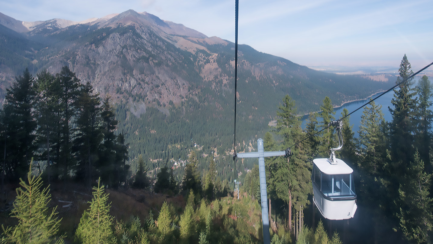 A view of the Wallowa Mountains, a part of Wallowa Lake and other tram cars making their way along a cabled route.