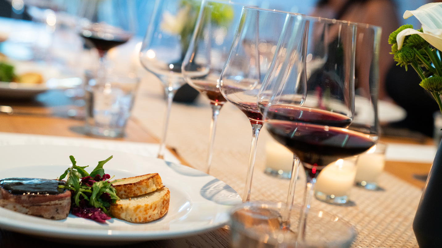 A plate of food and glasses of red wine on a table.