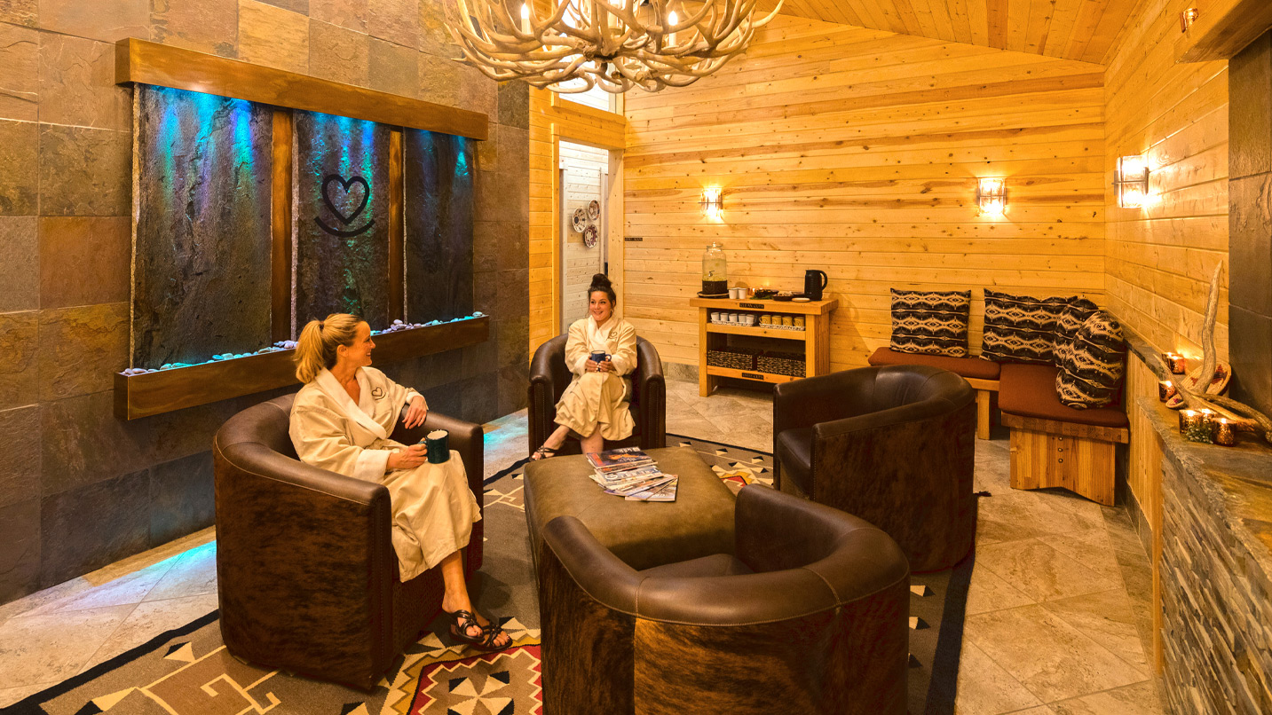 Two women sit in a log-cabin inspired lounge.