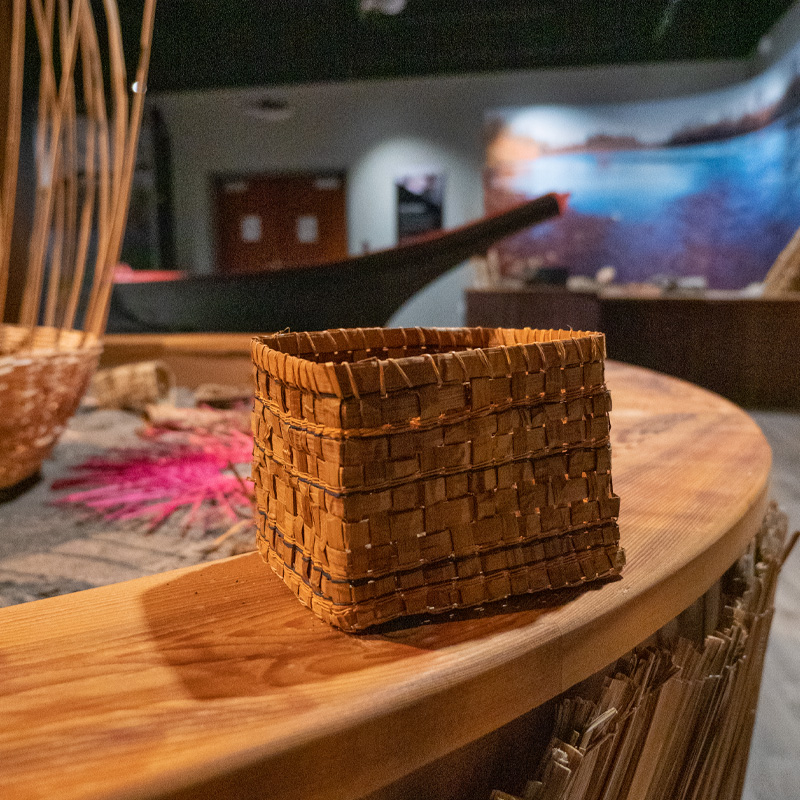 A hand-woven basket with a dug out canoe in the background.