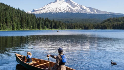 An adult and child canoe in a Mt. Hood-reflected lake.