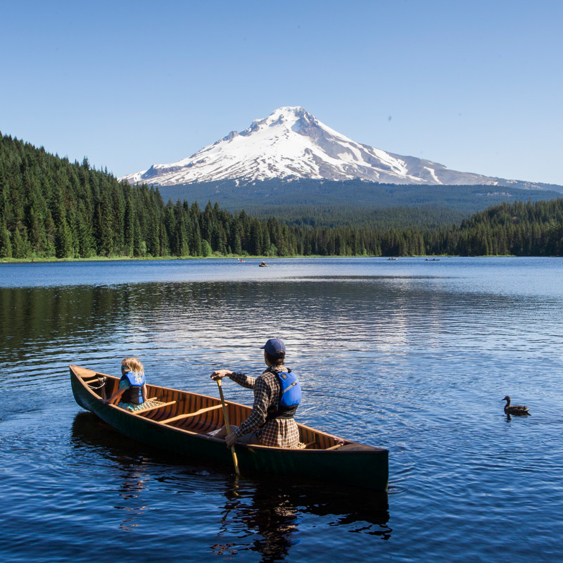An adult and child canoe in a Mt. Hood-reflected lake.